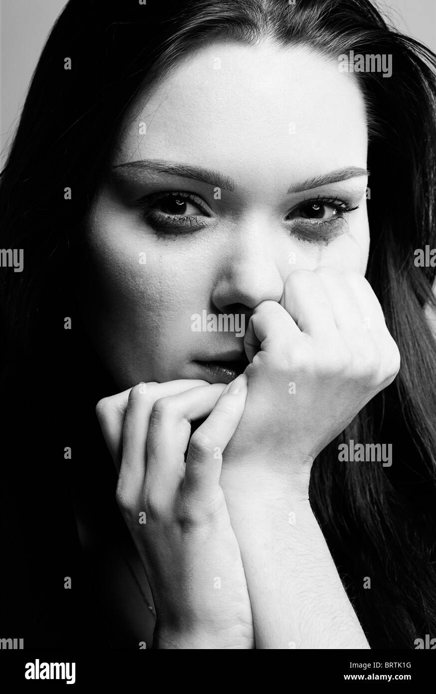 portrait of beautiful crying girl with smeared mascara hiding her face in hands Stock Photo