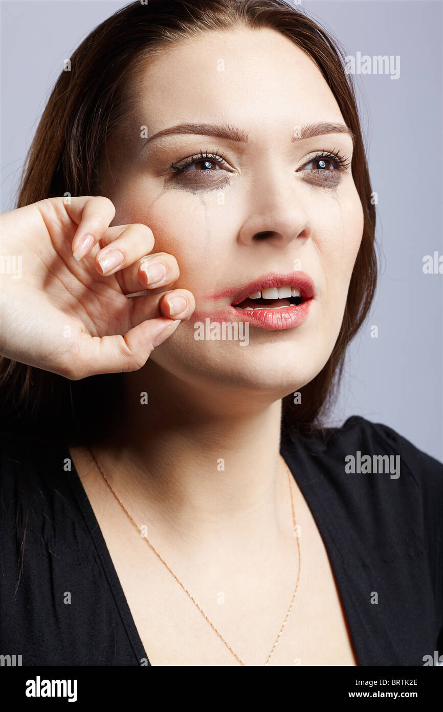 portrait of beautiful crying girl with smeared mascara drying her tears
