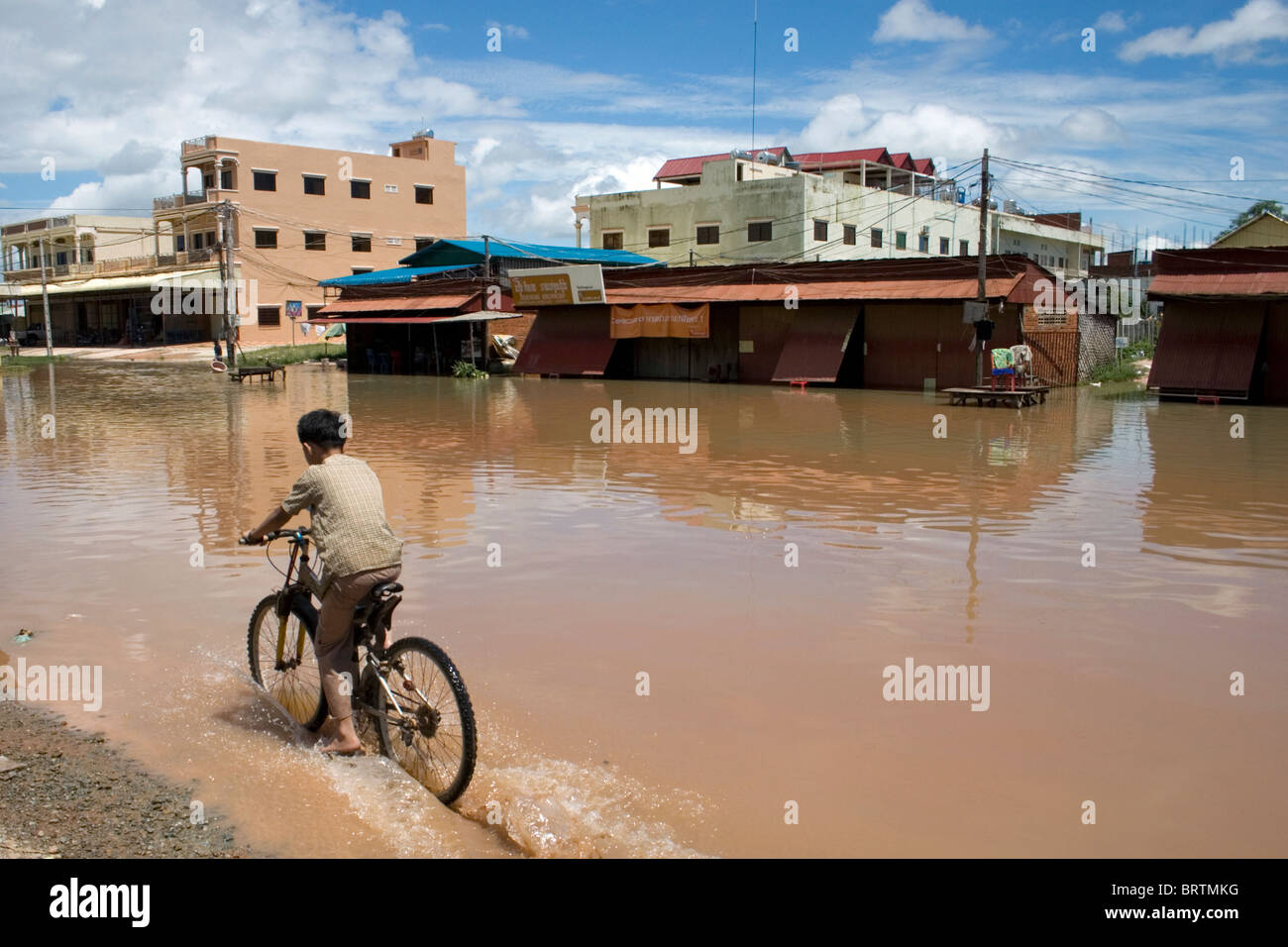 A boy on a bicycle rides through muddy water after the historic flood of 2009 in Siem Reap, Cambodia. Stock Photo
