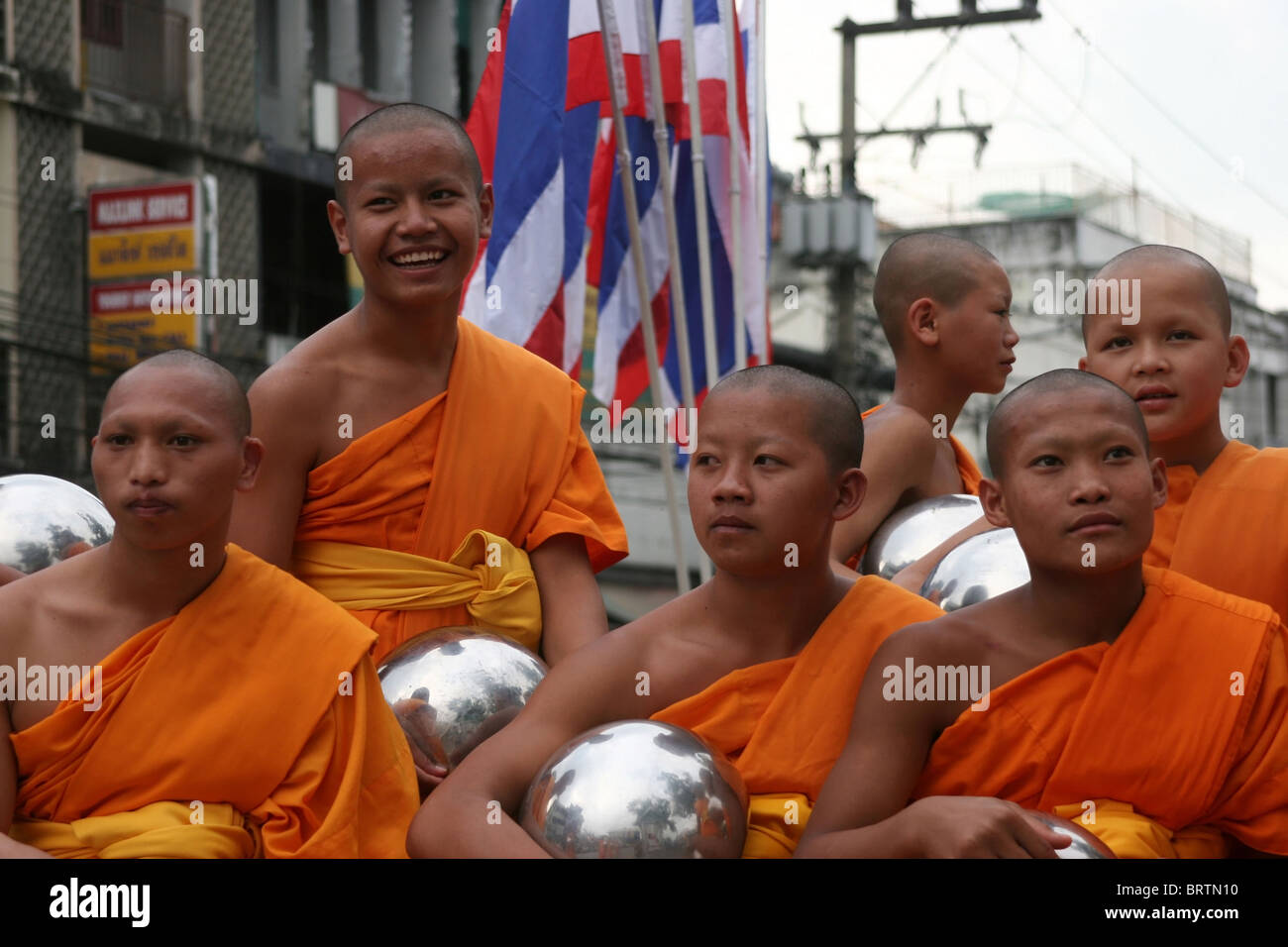 Buddhist monks wearing orange robes sit with their alms bowls near Tha