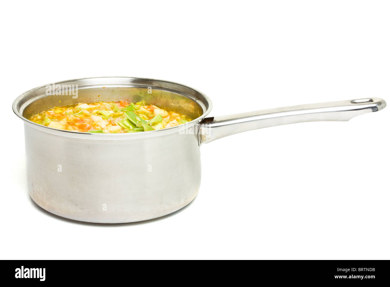 Rustic vegetable and ham broth in stainless steel saucepan isolated on white. Stock Photo