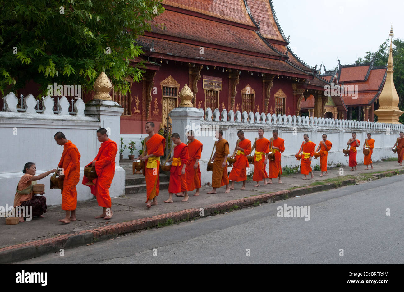 Row of monks gathering alms in front of wat siphouttabat thippharam , Luang Prabang. Laos Stock Photo