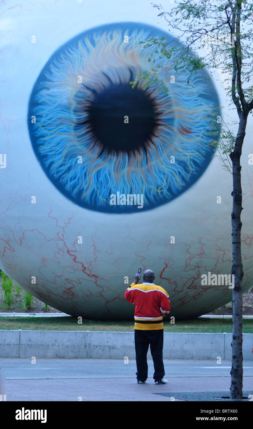 Tony Tasset's 'Eye' art piece with man standing in front of it taking a photo on his cell phone Stock Photo