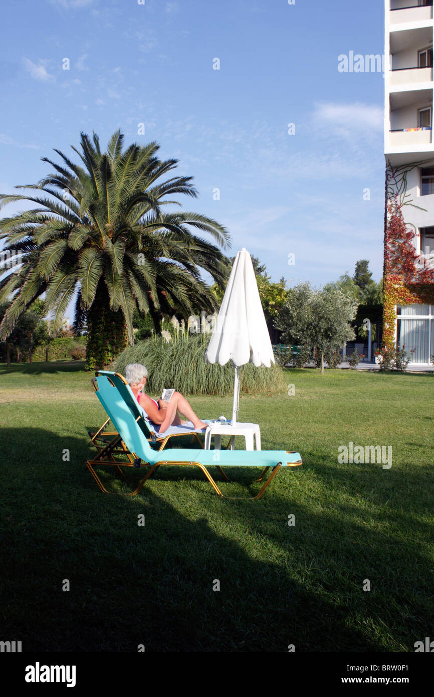 OLDER FEMALE HOLIDAYMAKER RELAXING IN A HOTEL GARDEN. Stock Photo