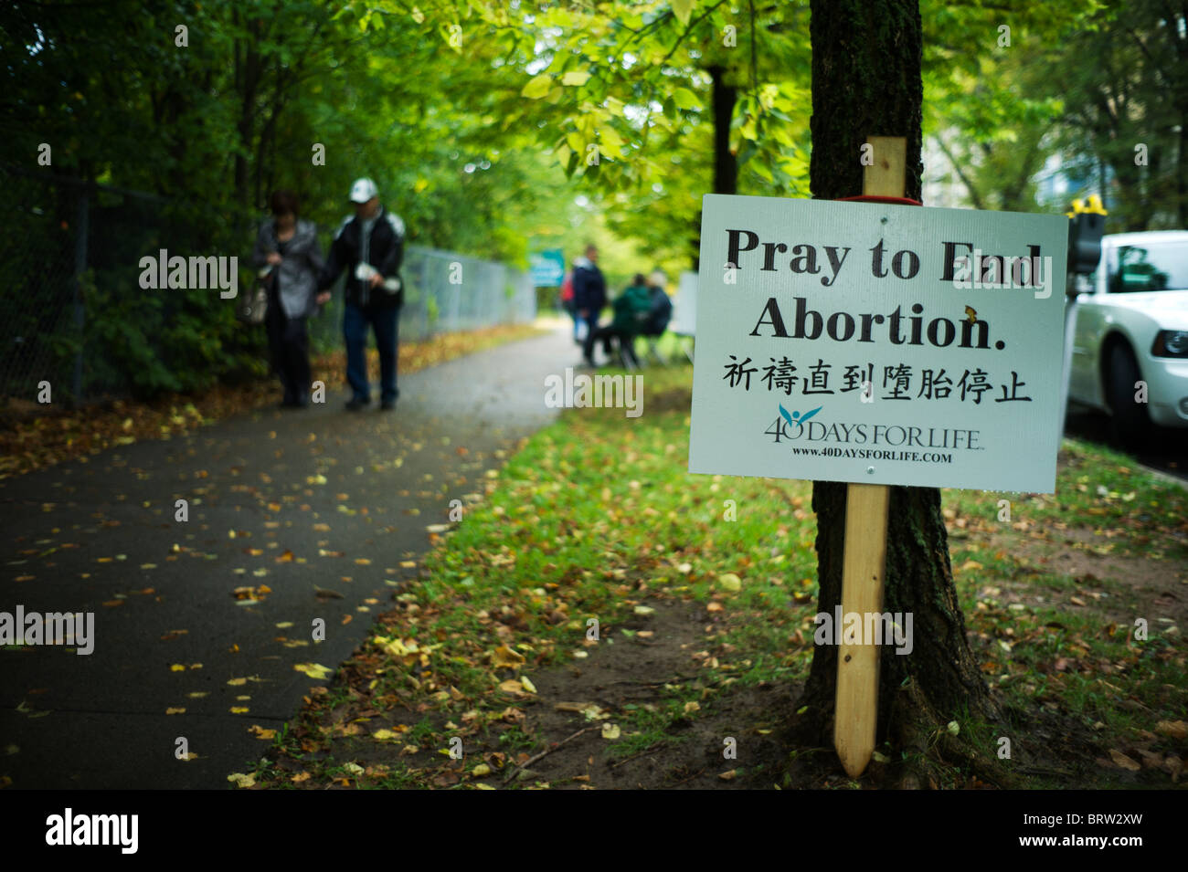 Anti-abortion sign and protesters on tree-lined sidewalk. Stock Photo
