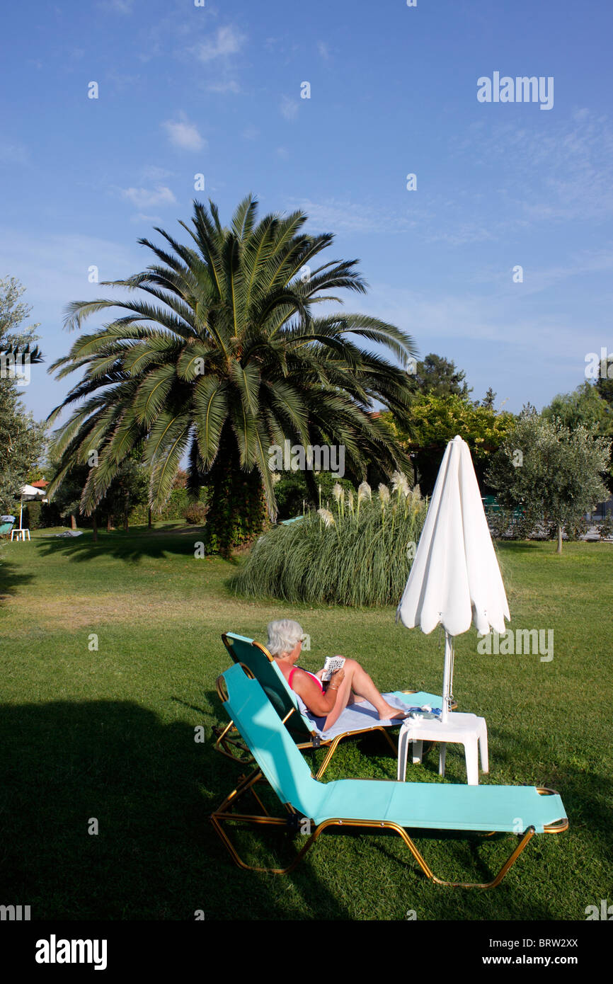 OLDER FEMALE HOLIDAYMAKER RELAXING IN A HOTEL GARDEN. Stock Photo