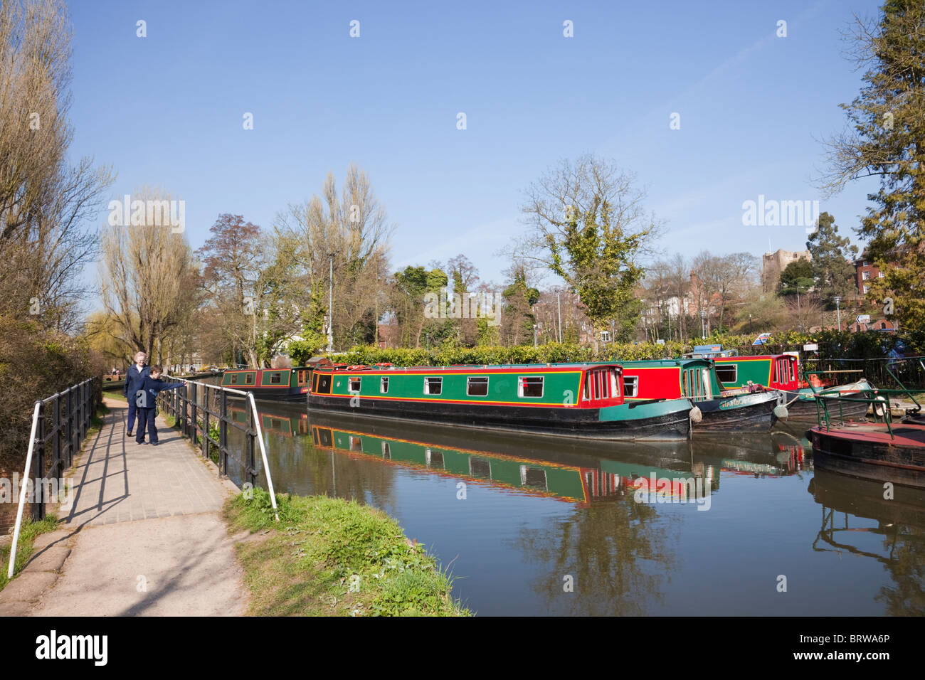 People walking on riverside path beside River Wey with canal boats moored on Godalming Navigation in Guildford Surrey England UK Stock Photo