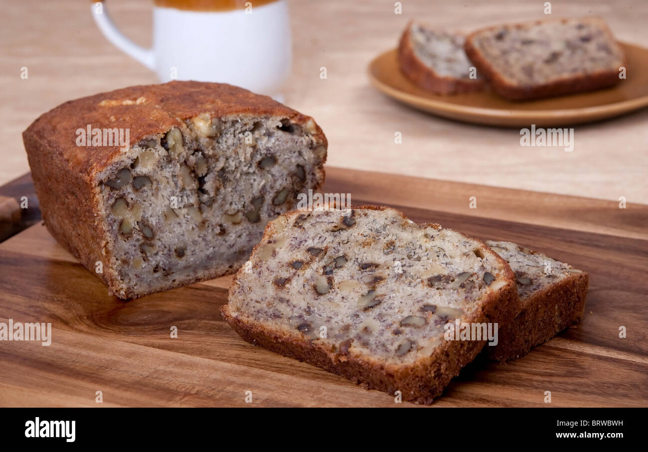 sliced loaf of banana walnut bread on a cutting board with one serving of two slices and a mug in the background Stock Photo