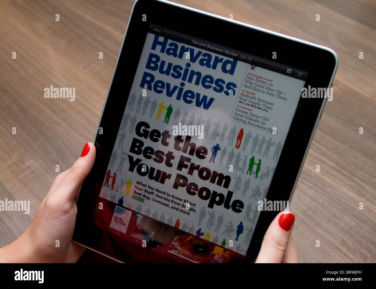 Woman's hands holding an Apple iPad with her reflection on the screen, showing Harvard Business Review Magazine. Stock Photo