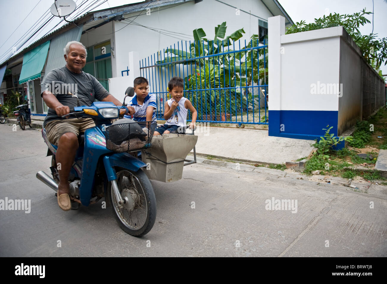 Young Thai brothers, ride in the makeshift sidecar on their grandfathers moped. Ban Hau Thanon, Koh Samui. Thailand Stock Photo