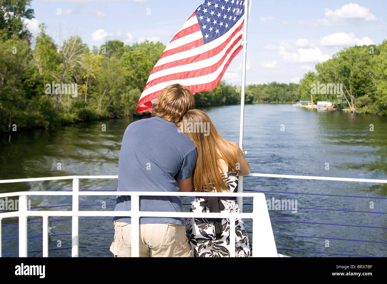 young cute couple holding each other on a boat with the American flag in the background Stock Photo