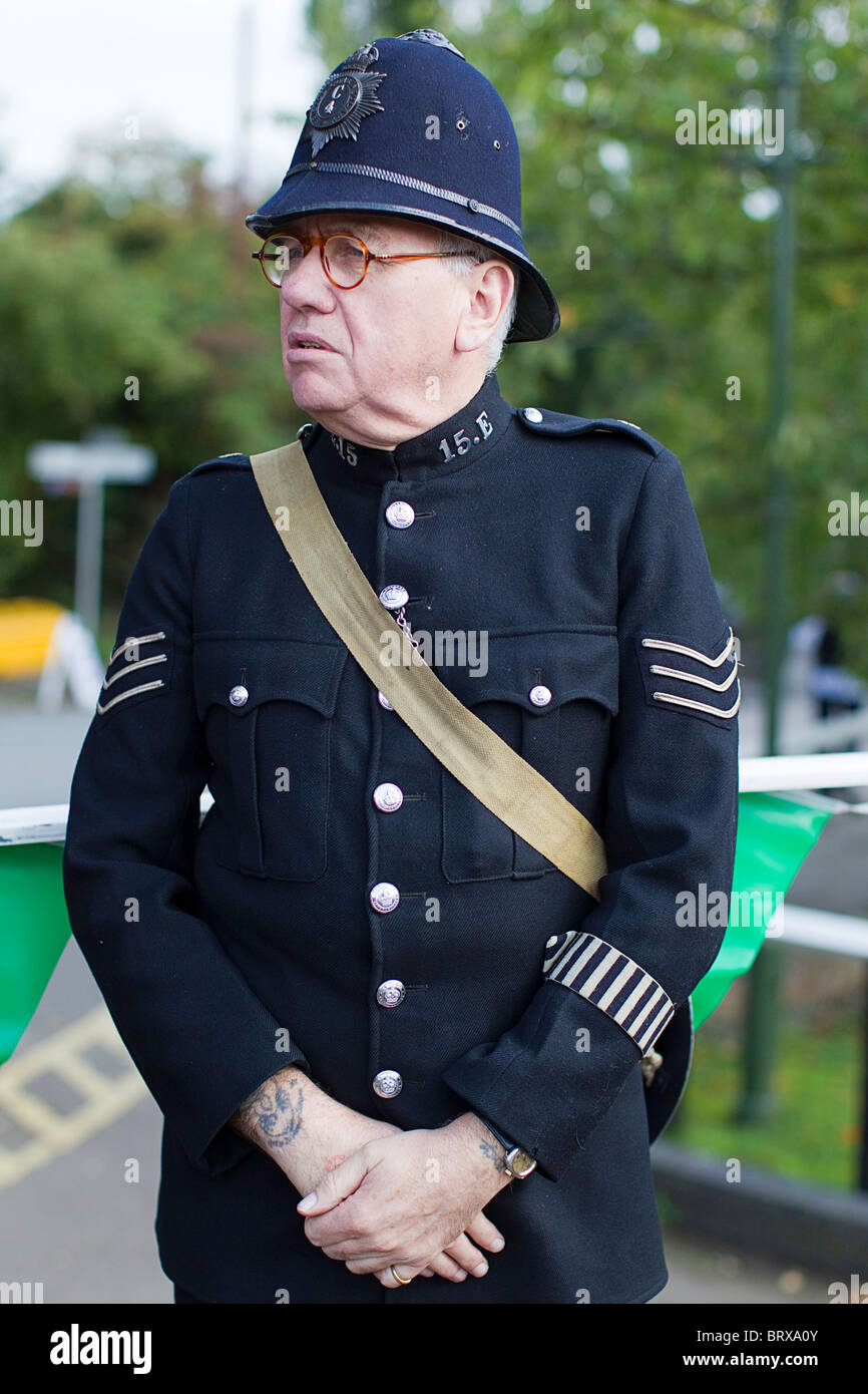 1940's War Years British Bobby Police Sergeant in Buttoned Blue Tunic with Sleeve Insignia & Custodian Helmet Stock Photo