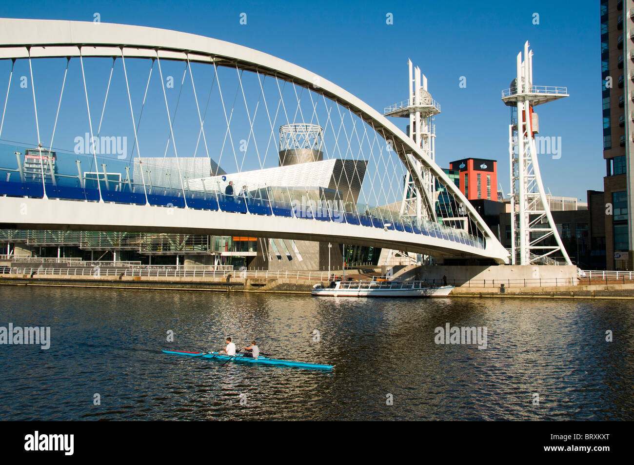 Sculling (rowing) on the Manchester Ship Canal, under the Millennium (Lowry) footbridge, Salford Quays, Manchester, UK Stock Photo