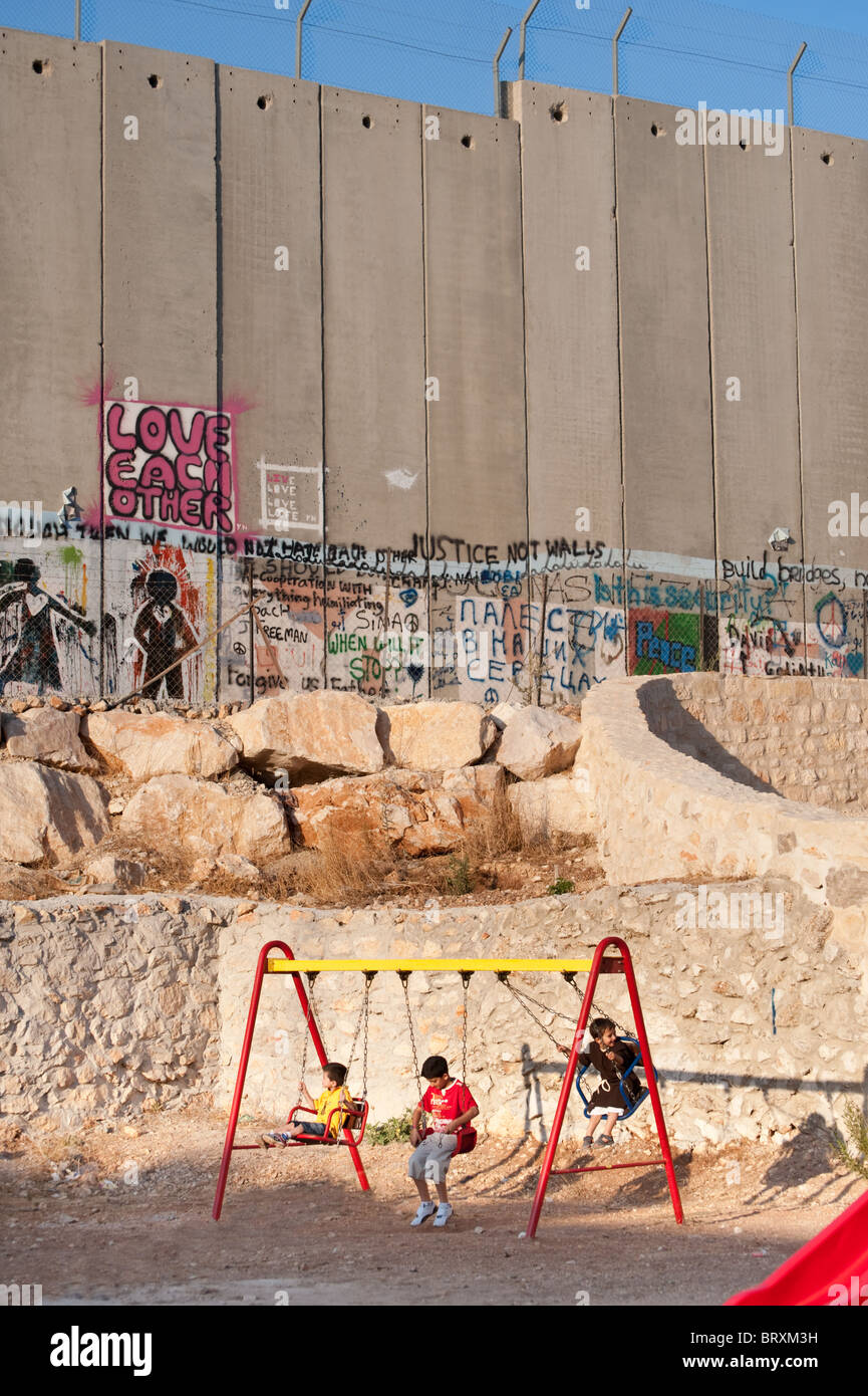 Next to the Israeli separation wall that divides the West Bank town of Bethlehem, Palestinian children enjoy a playground. Stock Photo