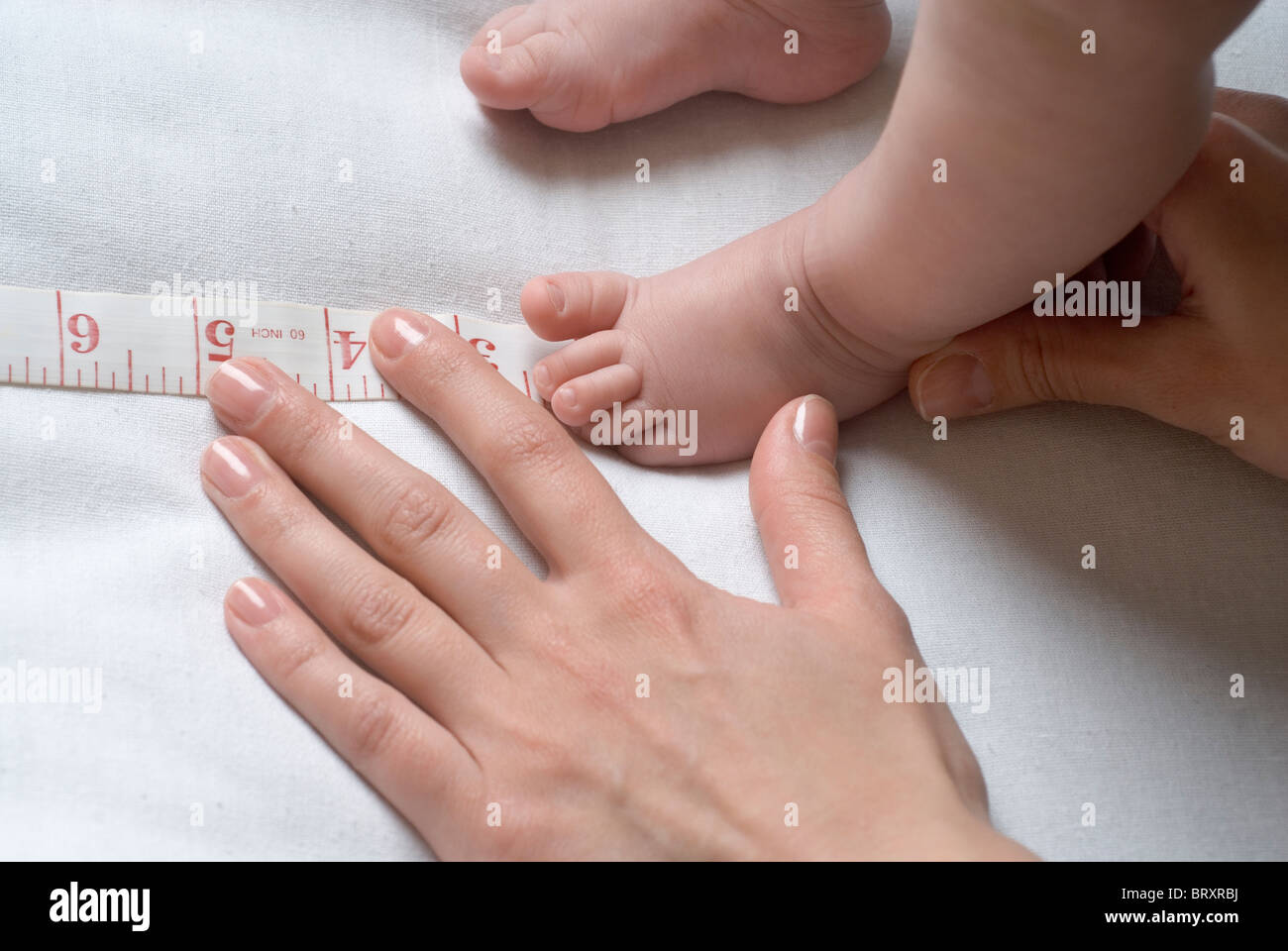 Mother measuring baby's (611 months) foot with tape measure Stock