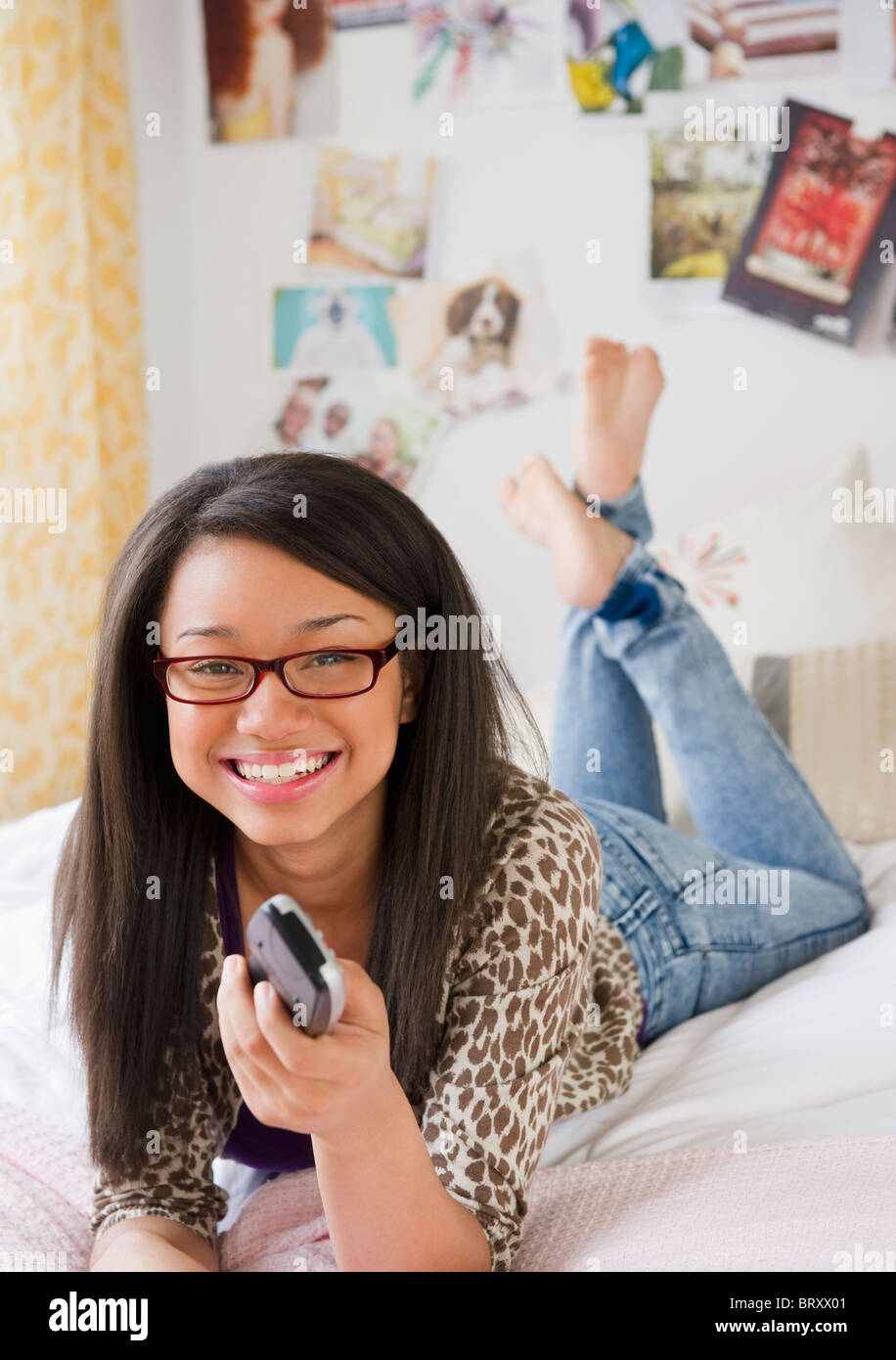 Mixed race teenage girl holding remote control and laying on bed Stock Photo