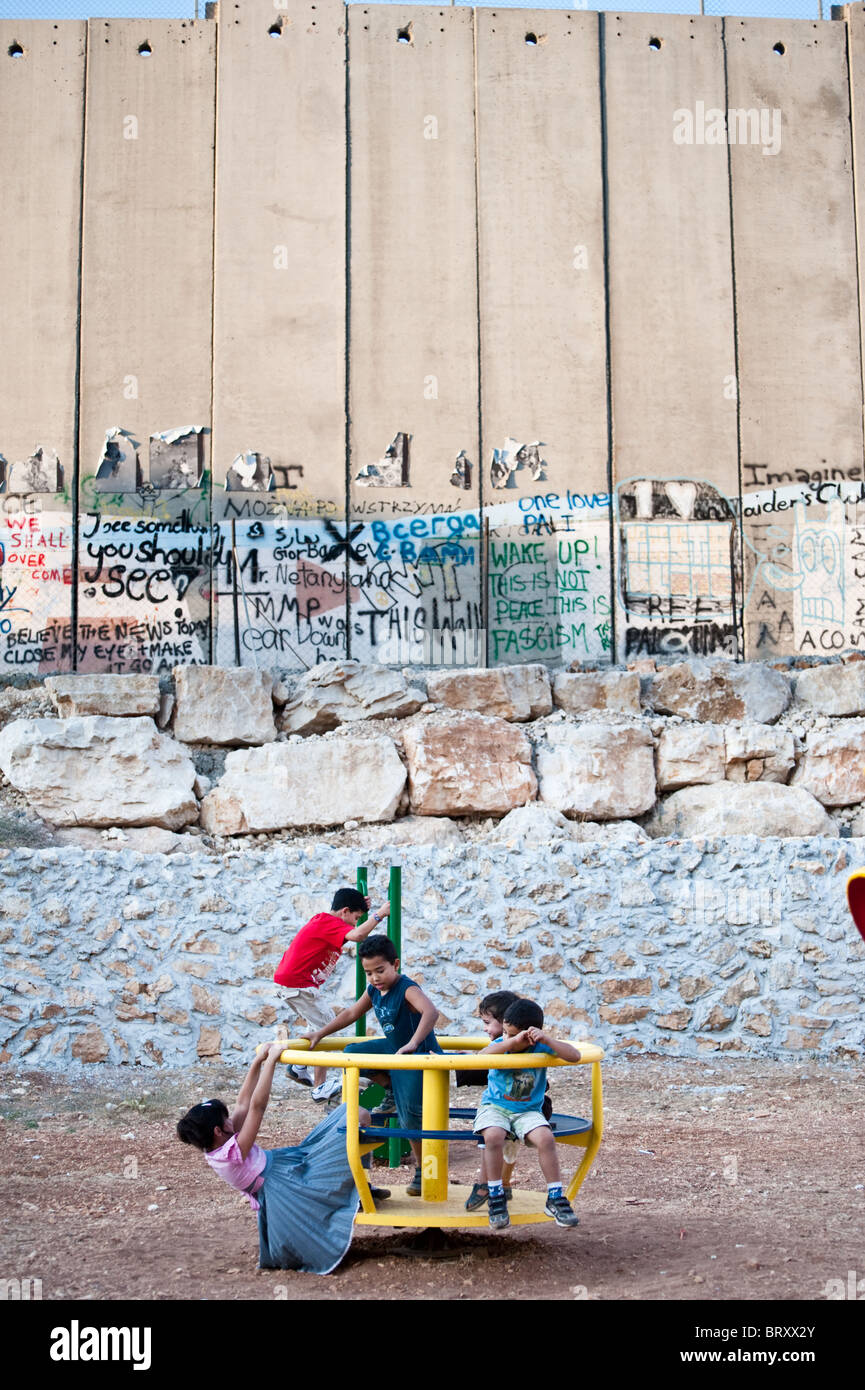 Next to the Israeli separation wall dividing the West Bank town of Bethlehem, Palestinian children enjoy a merry-go-round. Stock Photo