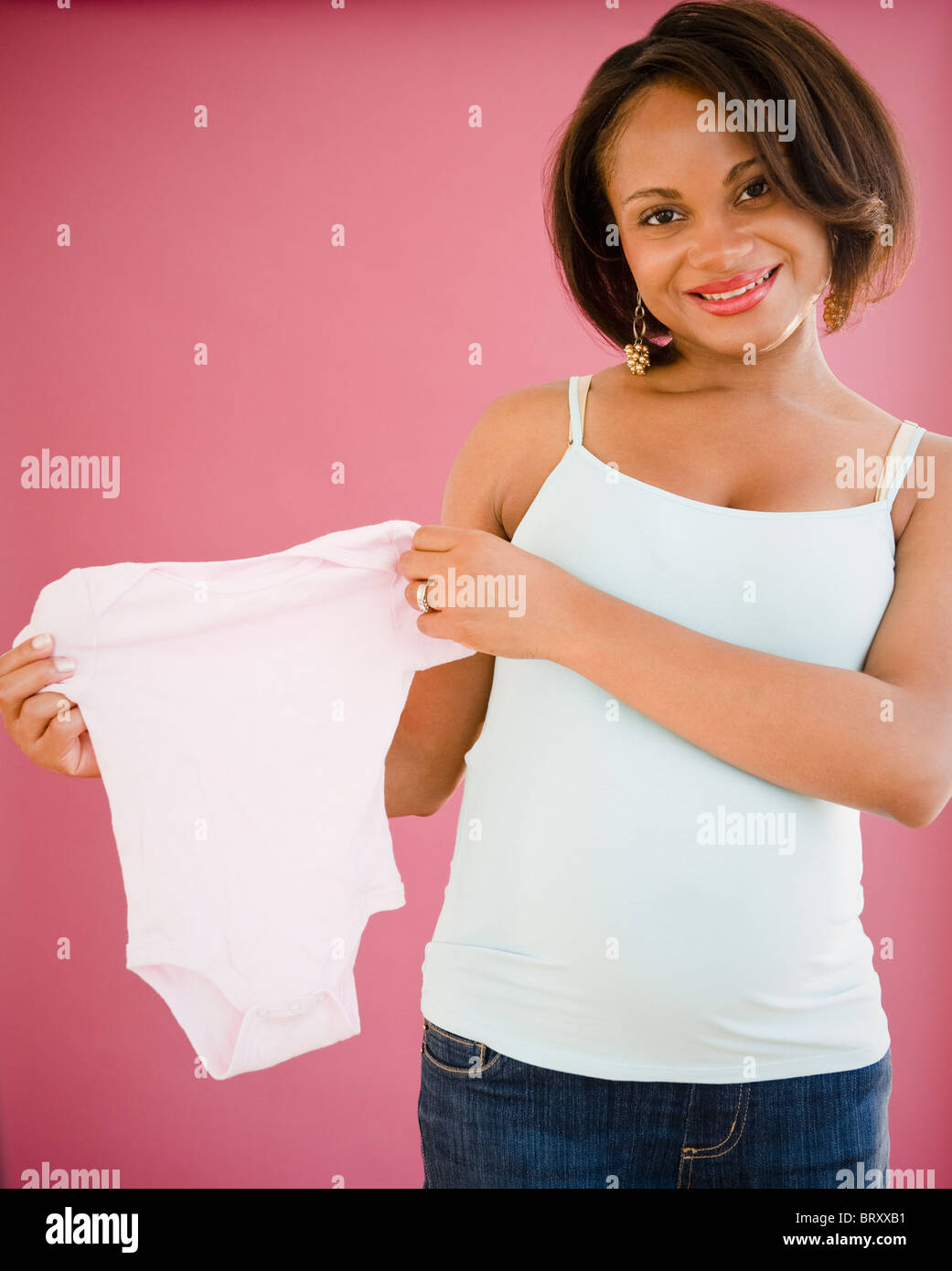 Smiling pregnant Black woman holding onesie Stock Photo