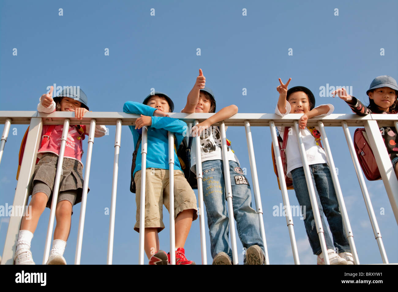 Boys and girls giving thumbs up and peace sign Low angle view Japan Stock Photo
