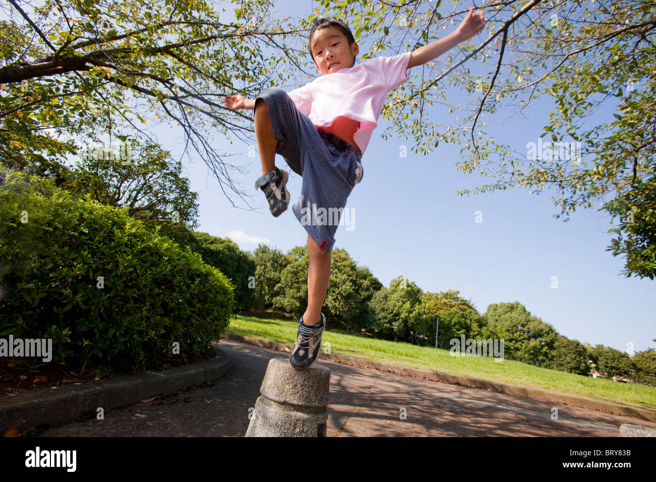 Boy standing on one leg on concrete  bollard, Japan Stock Photo