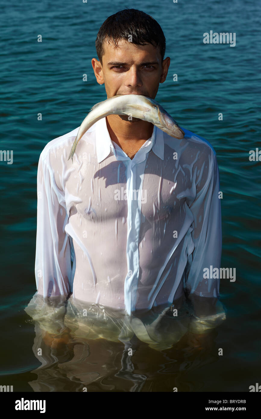 man in classic white shirt walking in water bearing fish in his mouth like  a predator Stock Photo - Alamy
