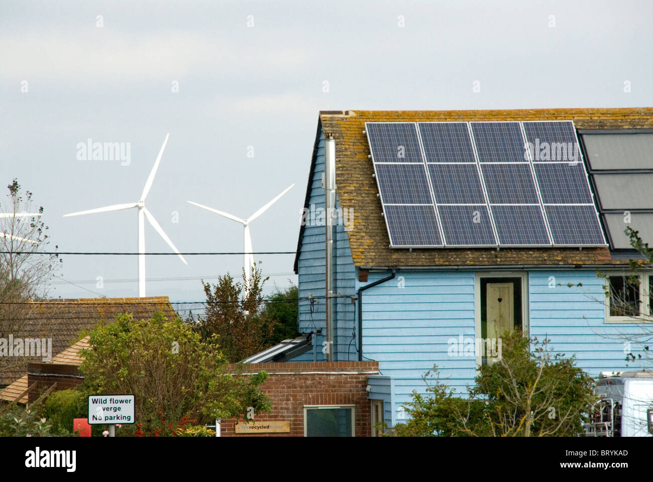 Wind turbines behind a house with solar panels The Recycled House