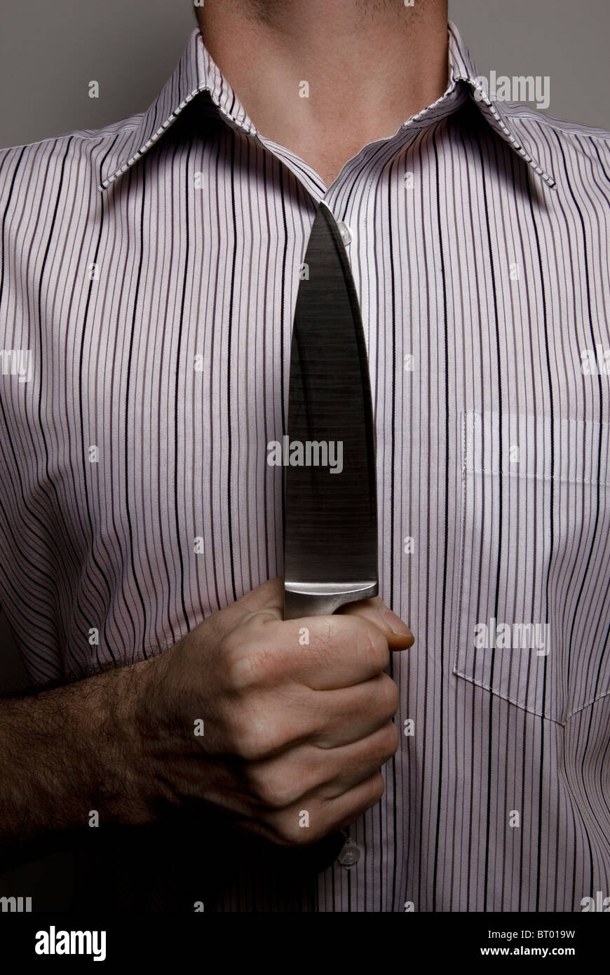 Close-up of man holding knife to chest in a threatening manner Stock Photo