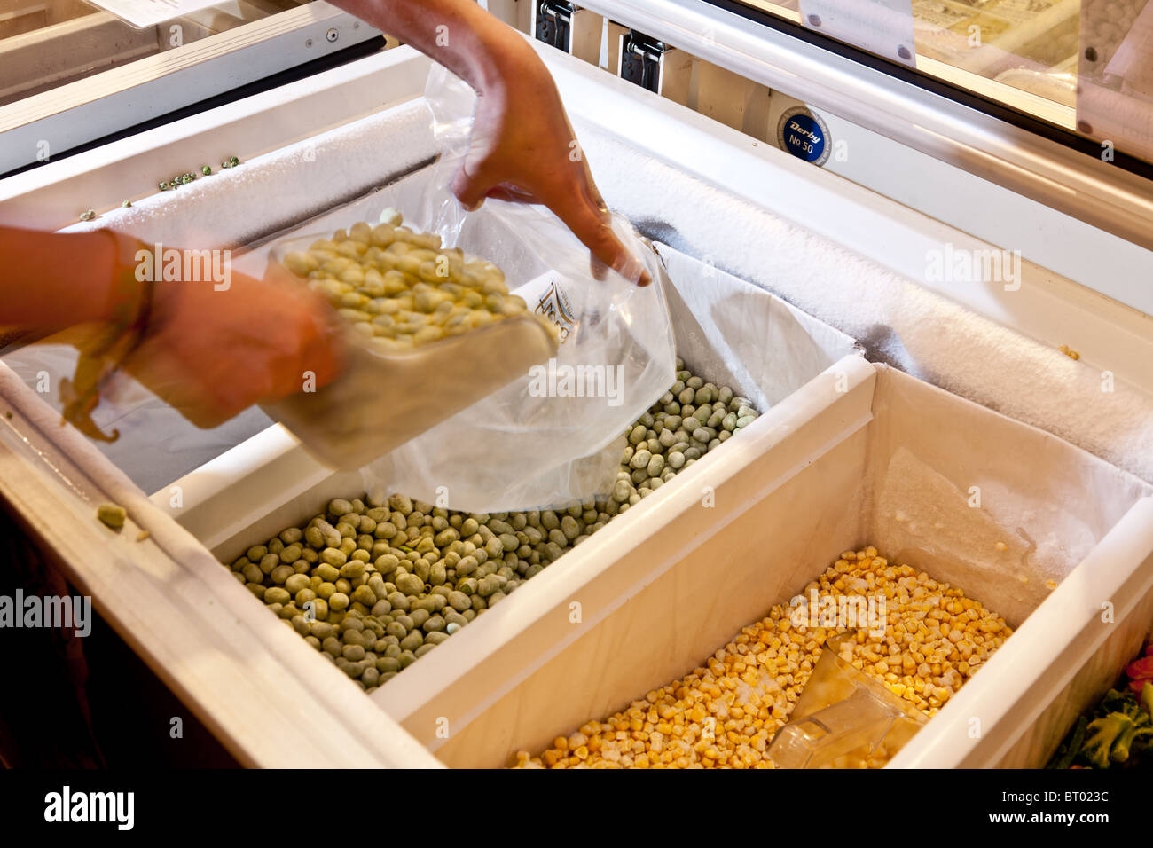 Shopper buying Loose broad beans from the freezer in a farm shop Stock Photo