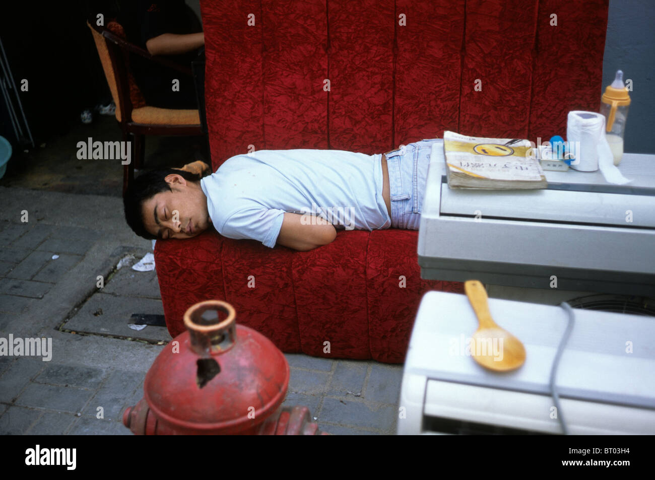 A tired  man lies on a sofa at his electrical domestic apliance repair service in Shanghai, China. 2009 Stock Photo