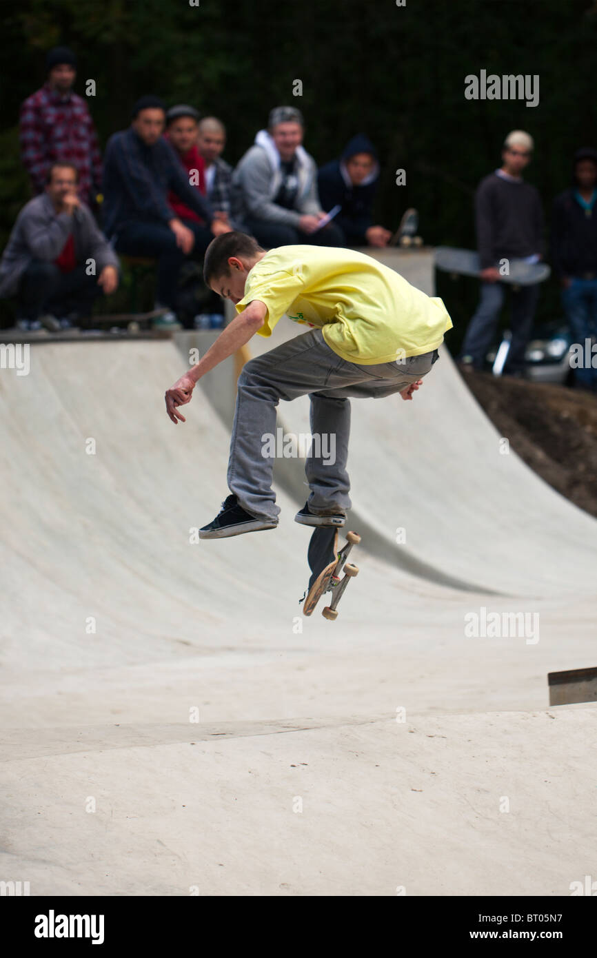 young skateboarder performing a jump, spectators sitting at the edge of halfpipe Stock Photo