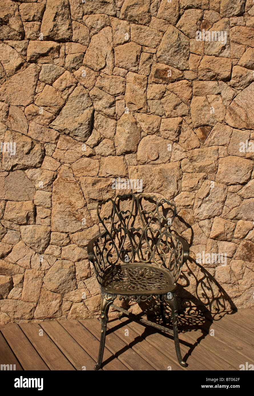 Rock wall and wooden deck with an empty chair Stock Photo