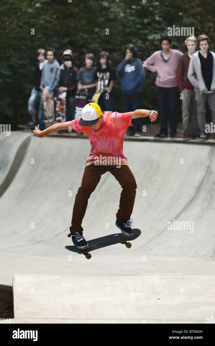 young skateboarder performing a jump, teenagers standing at the edge of halfpipe watching Stock Photo