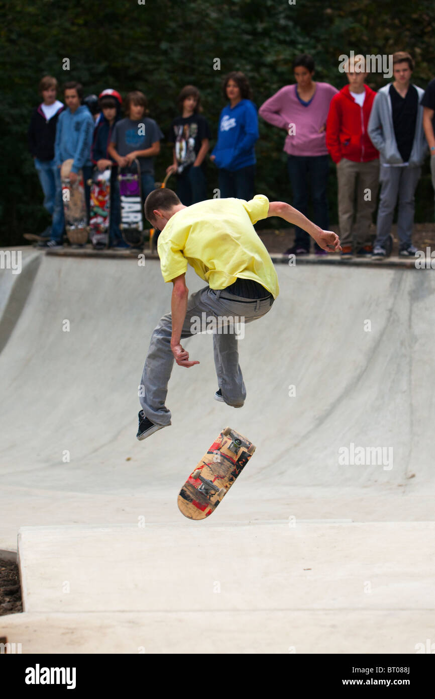 young skateboarder showing trick, being watched by other teens standing at the edge of halfpipe Stock Photo