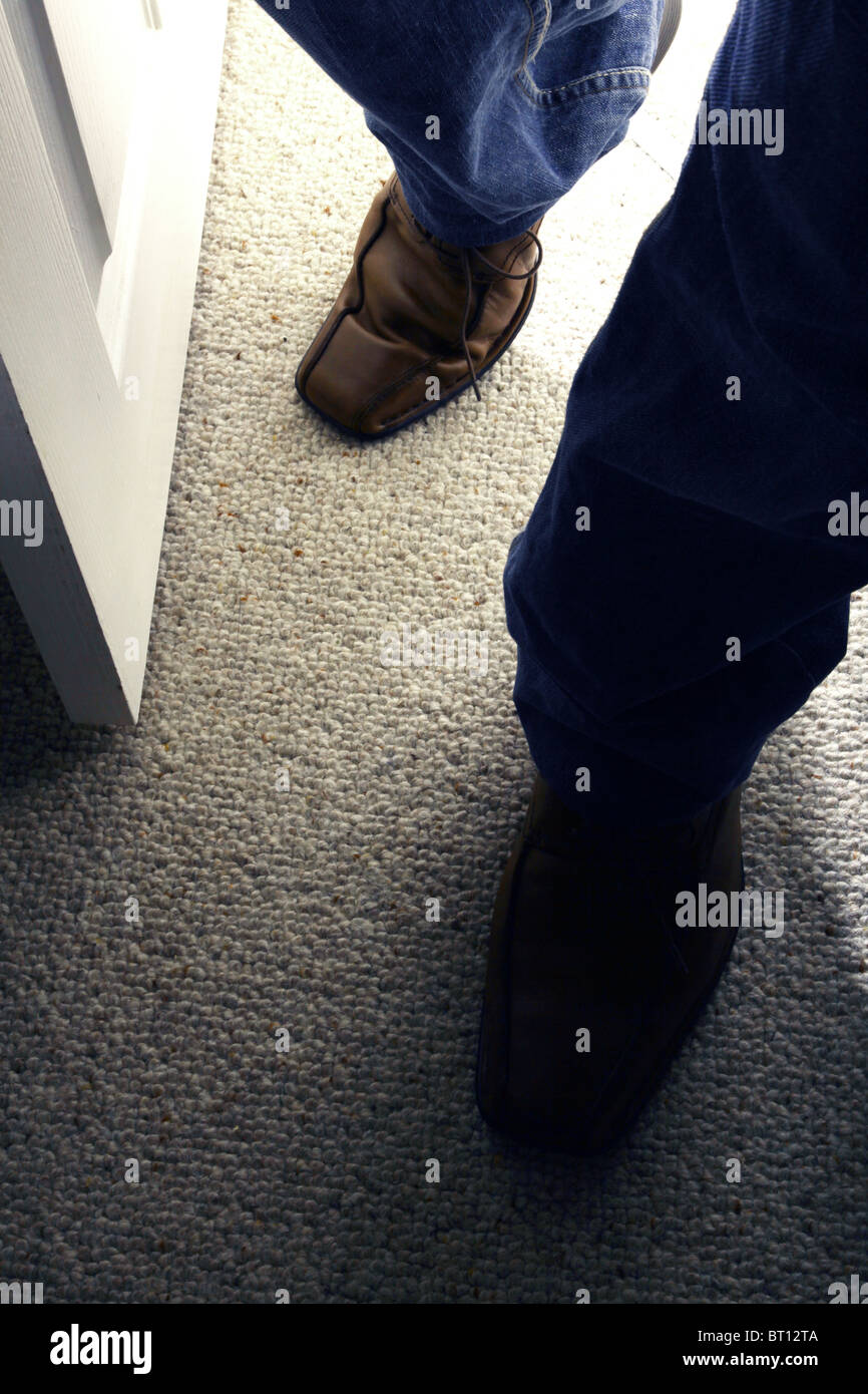 Male feet entering a dark room. Brown shoes. Stock Photo