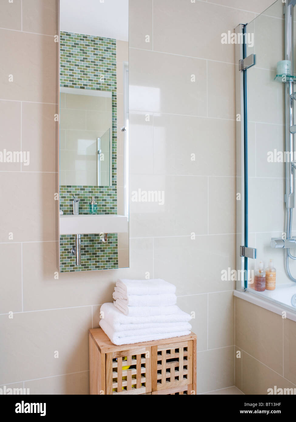 Pile of white towels on pale wood cupboard below long mirror in modern