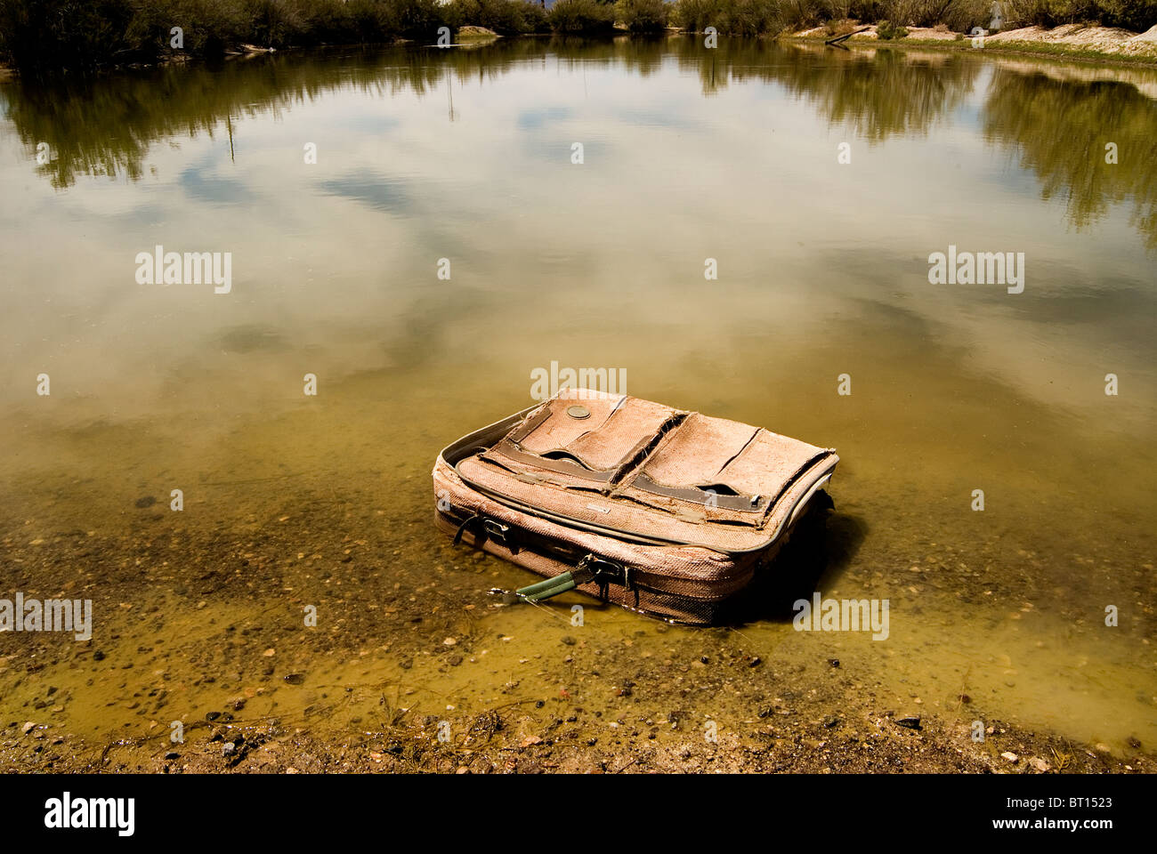 Old American Flyer travel suitcase discarded in the lake.Trashed suitcase. Lost dream. No plans. Travel luggage left behind. American Flyer bag. Stock Photo