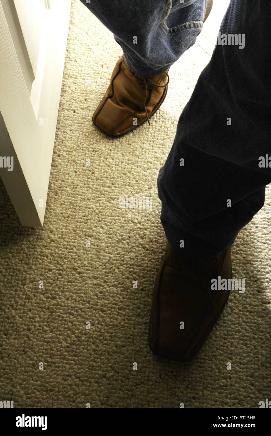 Male feet wearing brown shoes entering a dark room. Stock Photo