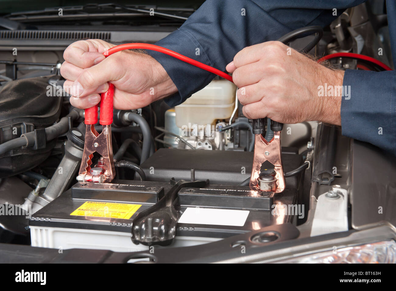 A car mechanic uses battery jumper cables to charge a dead battery. Stock Photo