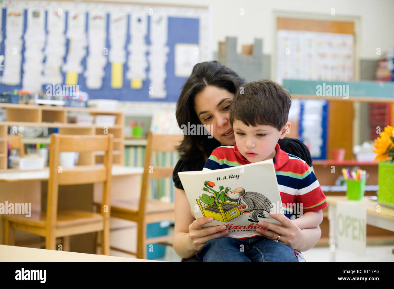 Hispanic teacher's aide reads to a 4 year old male in preschool. Stock Photo