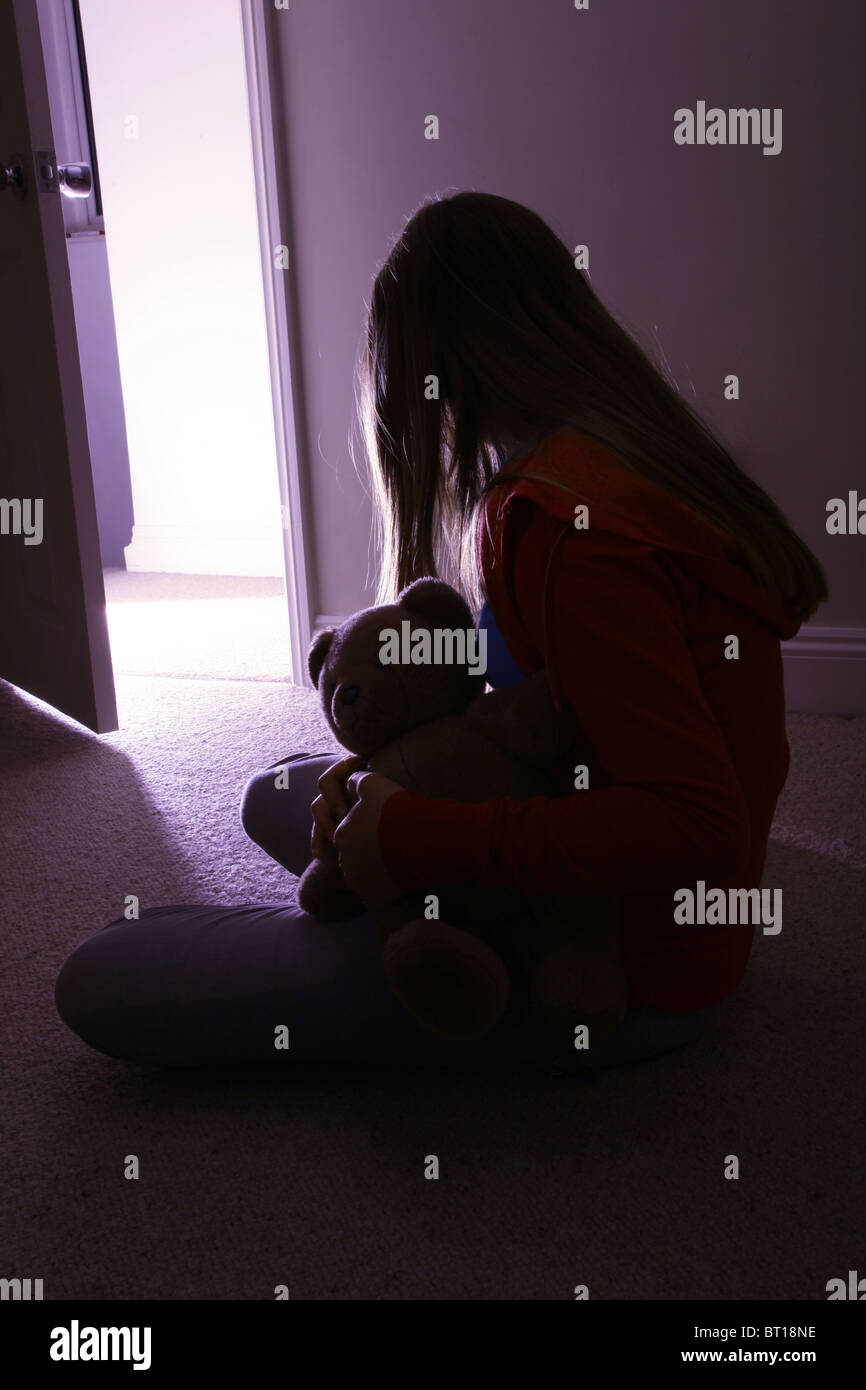 Child in a dark room alone holding a teddy bear, back view Stock Photo