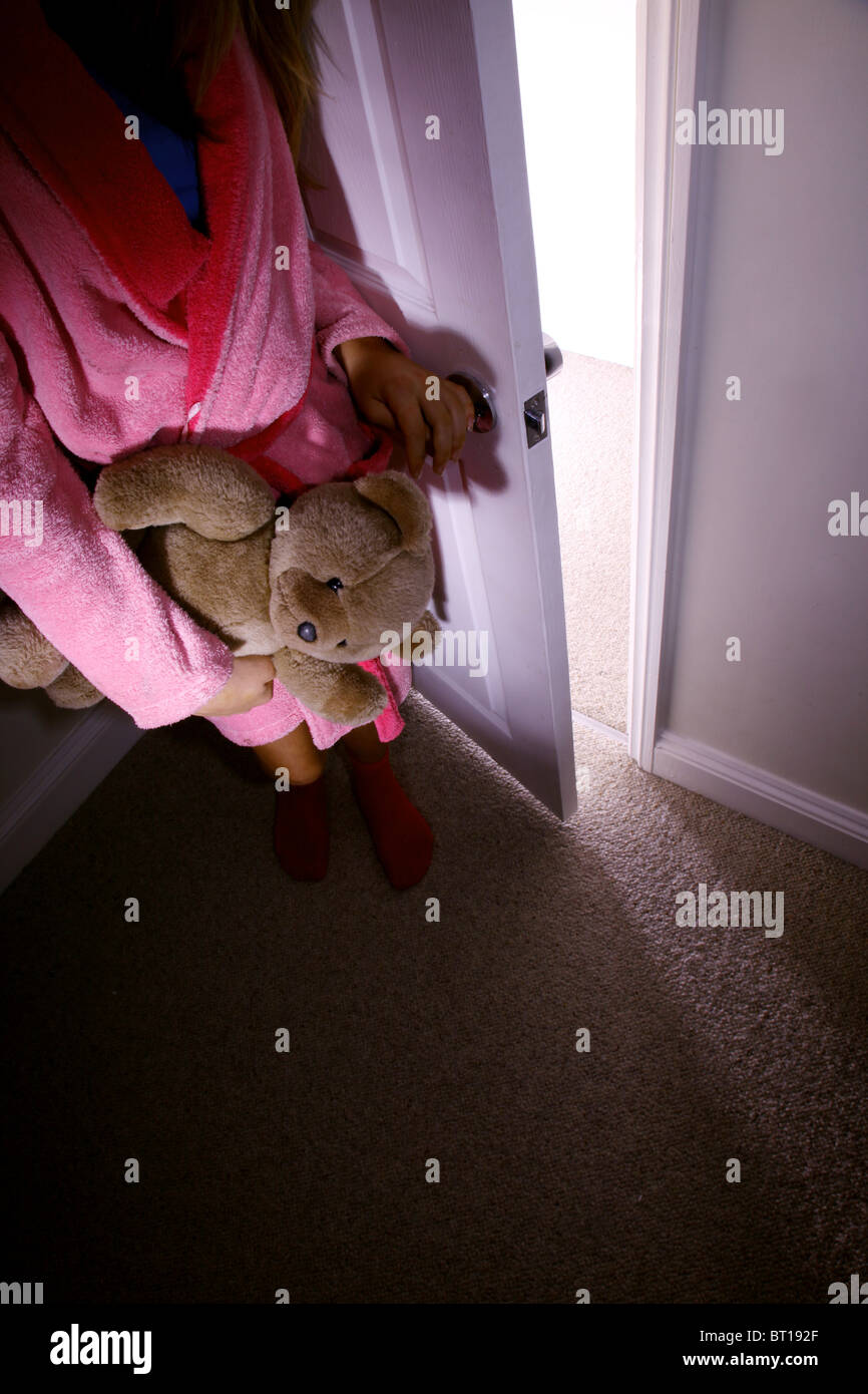 Child in a dark room alone holding a teddy bear Stock Photo
