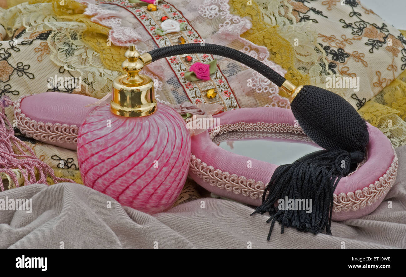 Closeup of pink perfume atomizer with hand mirror and lace purse decorated with lace, ribbons, embroidery. Stock Photo