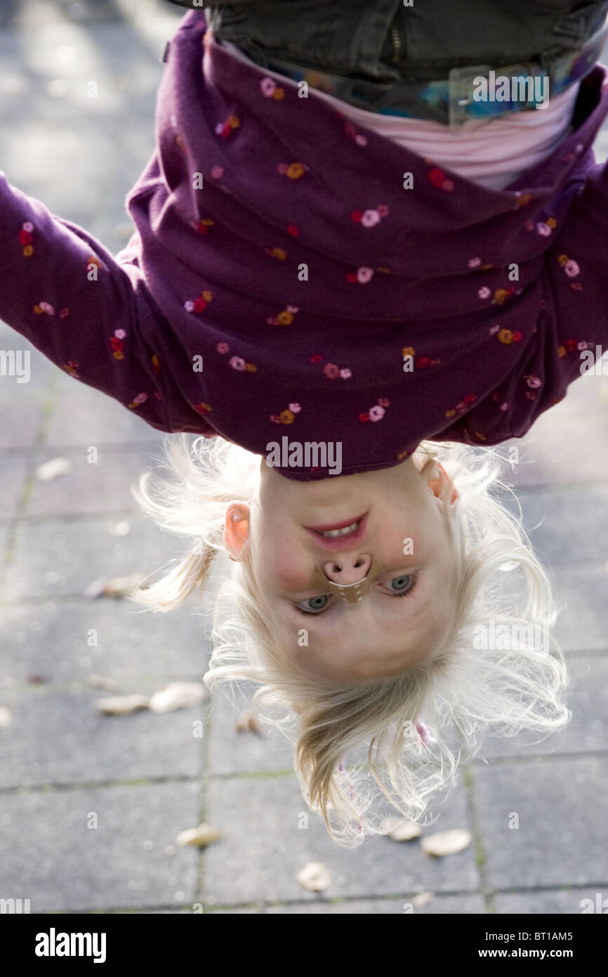 Child with blister on nose hanging upside-down in playground - Stock Photo