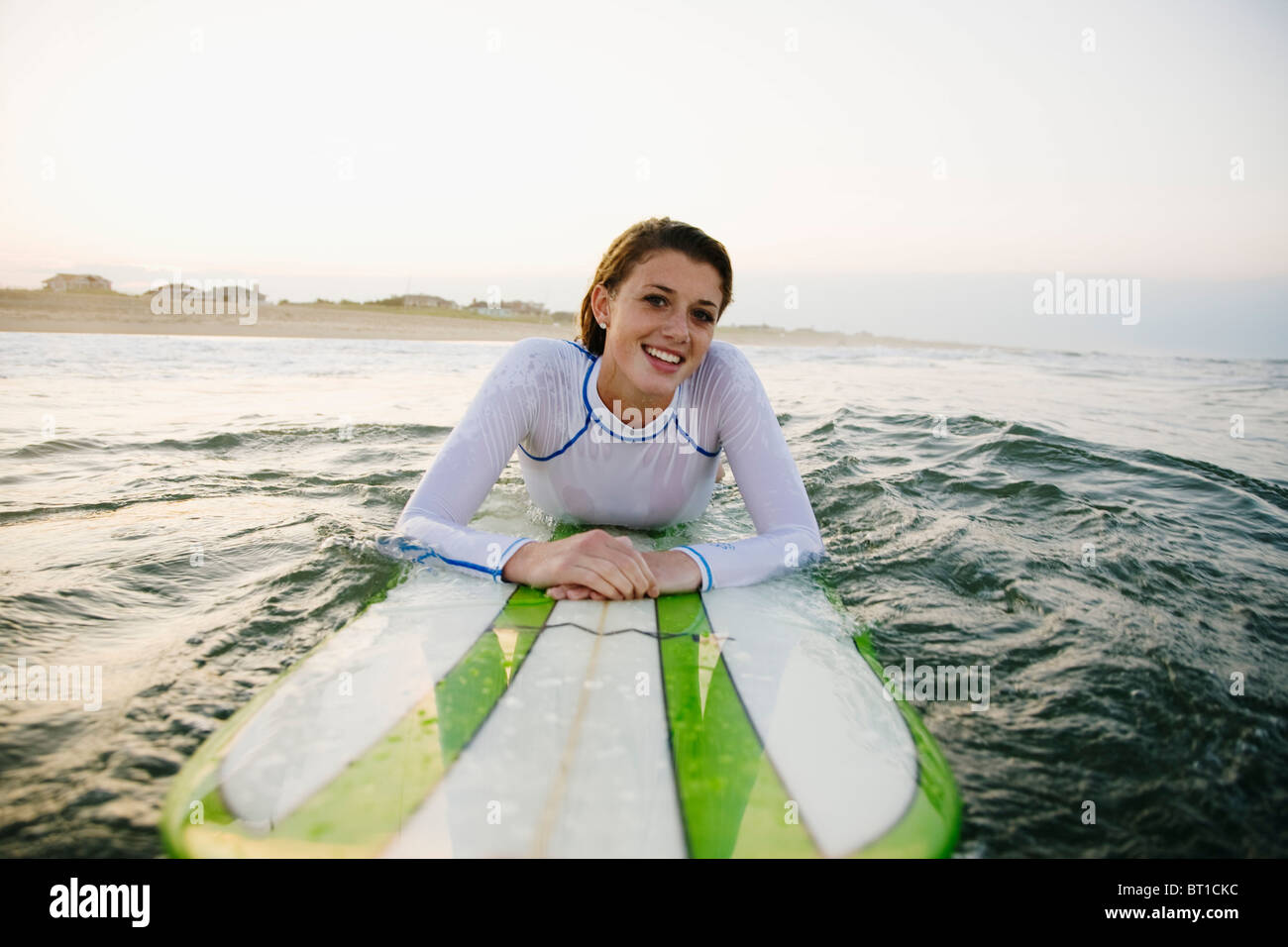 Smiling Caucasian teenage girl leaning on surfboard in ocean Stock Photo