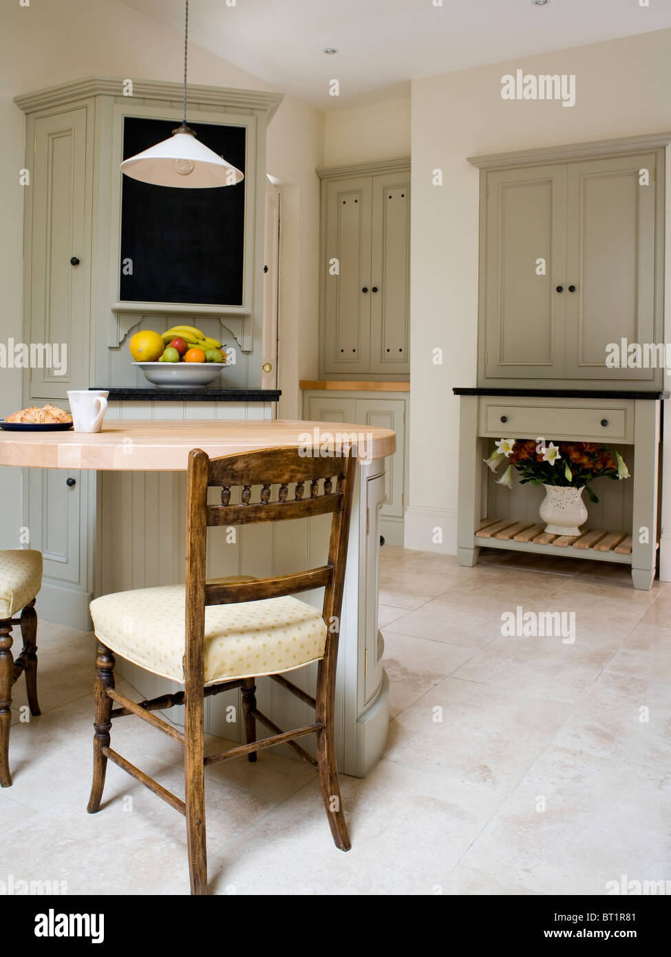 Antique Chairs At Breakfast Bar In Modern Kitchen With Limestone Flooring And Pale Gray Fitted Units Antique Chairs At Breakfast Bar In Modern Kitchen With Limestone Flooring And Pale Gray Fitted Units