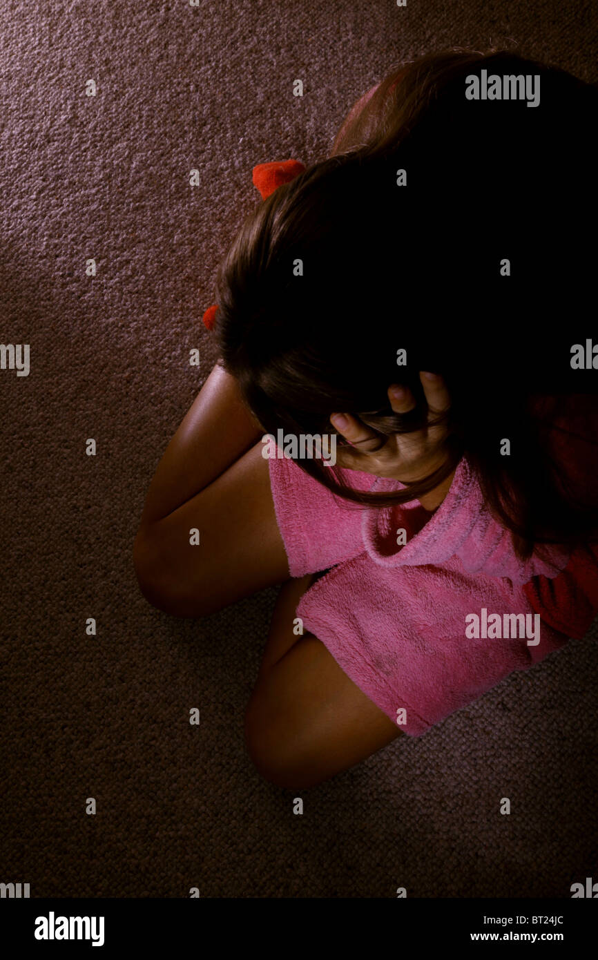 Girl wearing a dressing gown, sitting on a carpeted floor with her head in her hands. Stock Photo