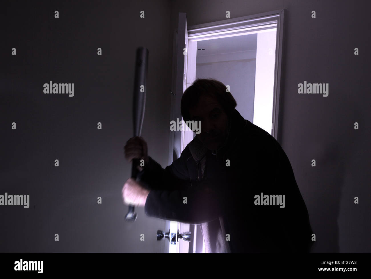 Male silhouette entering a dark room holding a baseball bat Stock Photo