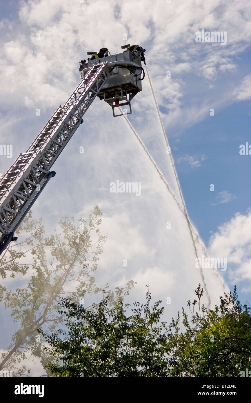 Firefighters training from ladder on ladder truck, with hoses, New