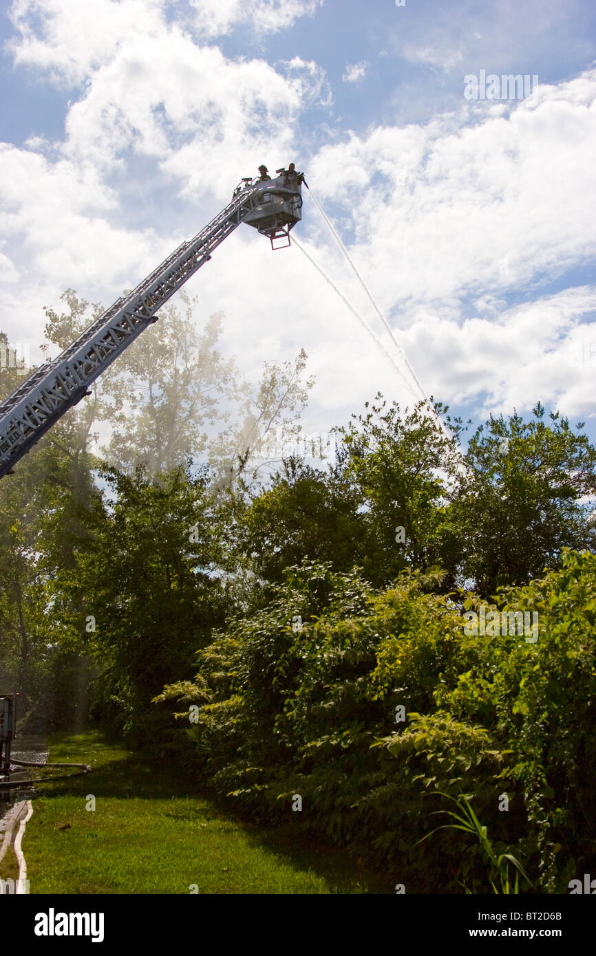 Firefighters training from ladder on ladder truck, with hoses, New