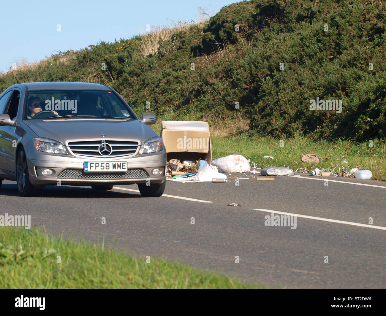 Car driving around rubbish which had fallen of back of lorry, UK Stock
